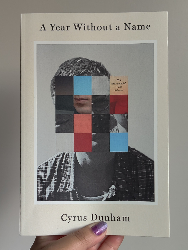 A book on a white background. The cover of the book has the title at the top "A Year Without a Name". There is the image of a person with squares superimposed on top of the face, which is also shifted so the top of the head doesn't align with the bottom. Each square has a different image or color, black square, blue square, grey square, a square with "An anti-memoir" -- The Atlantic, squares with lips or eyes. It says Cyrus Dunham at the bottom. 